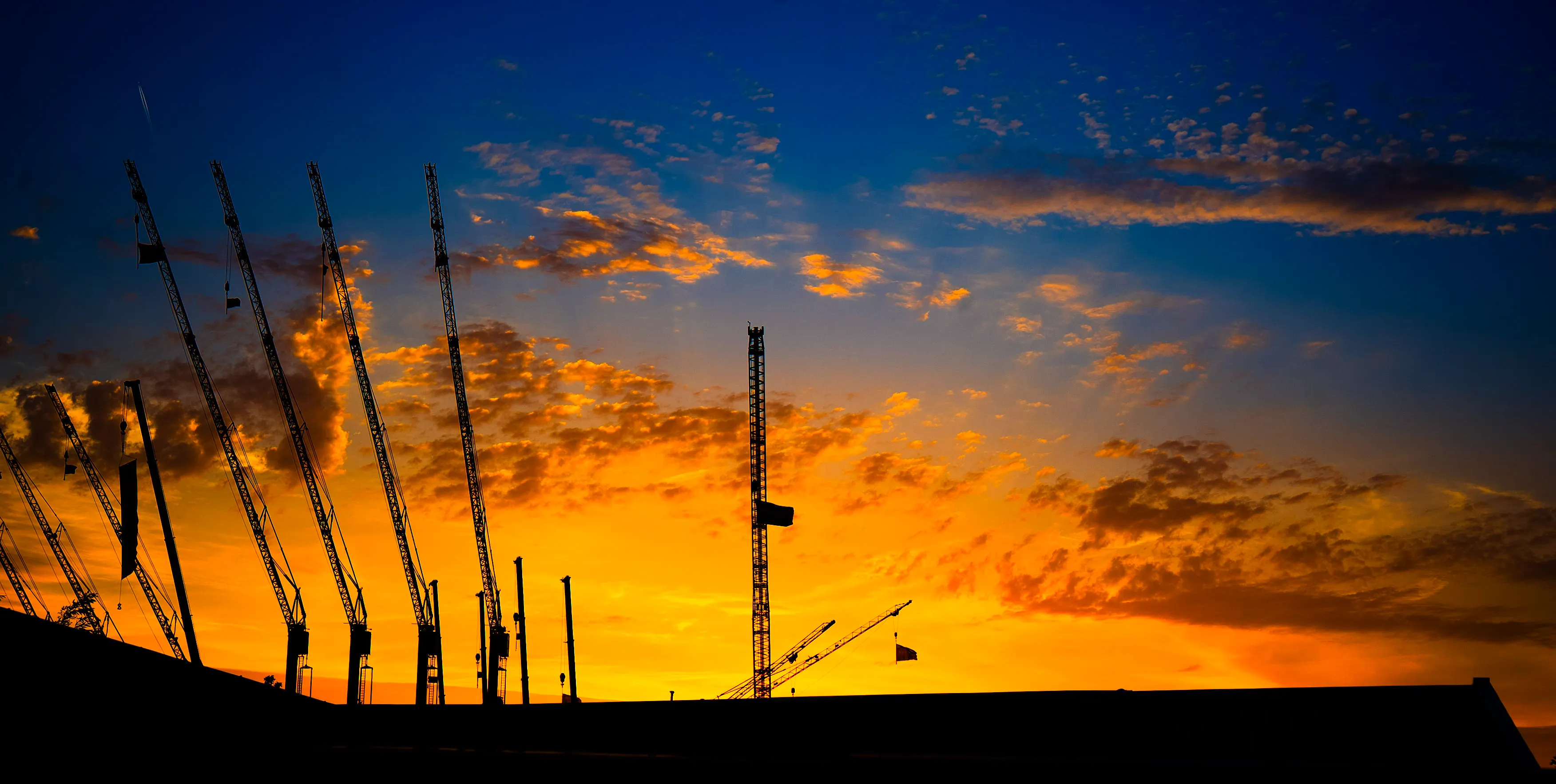 Silhouetten van bouwkranen tegen een kleurrijke zonsondergang